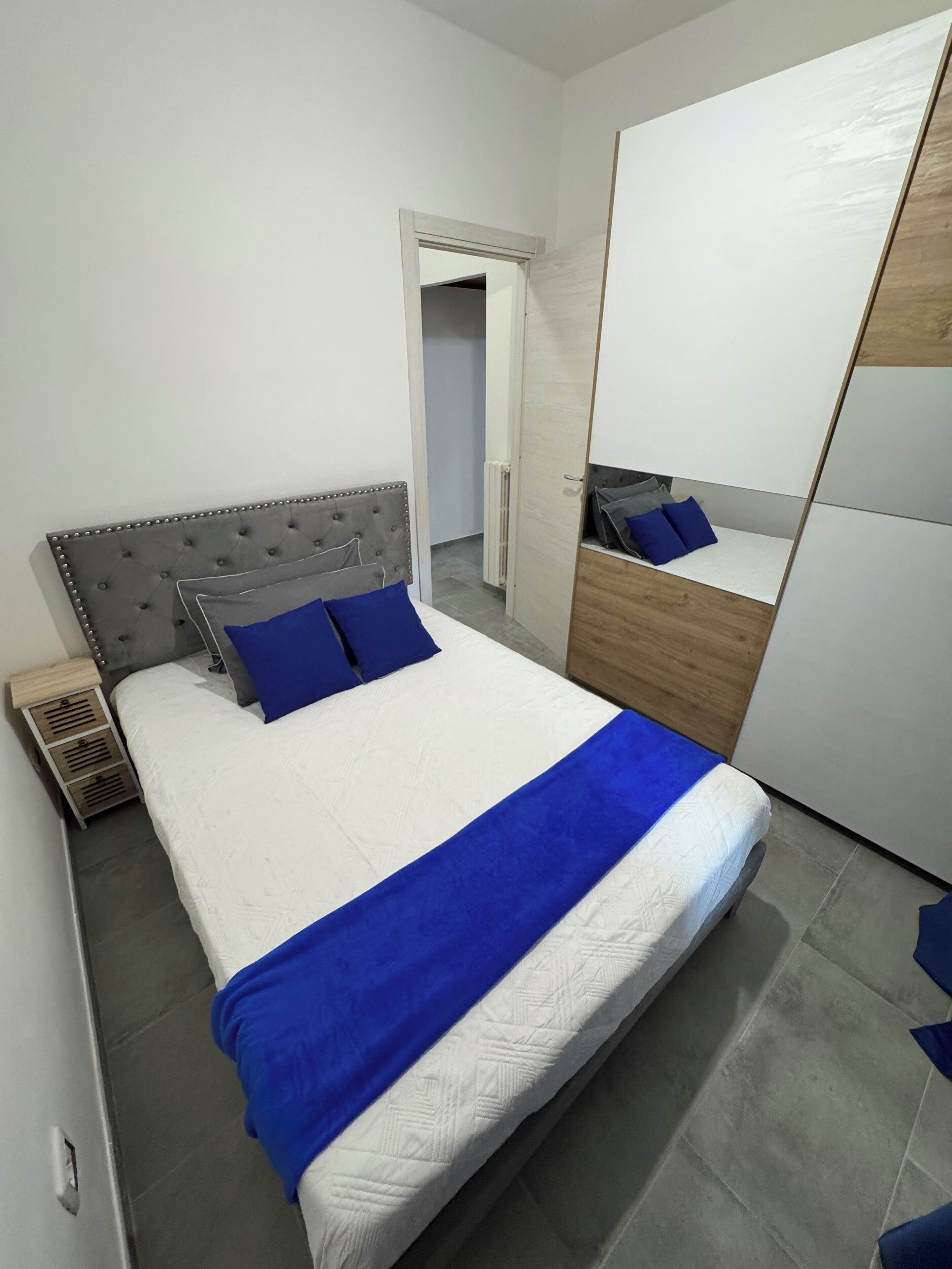 A neatly arranged bedroom with a large bed, a bedside table, a wardrobe, and a mirror.