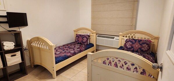 A bedroom with two single beds, a TV, a shelf with folded towels, and an air conditioning unit. - Enjoy in Charming Place, 3-bedroom, 2 bathroom with AC in Río Grande (Río Grande)