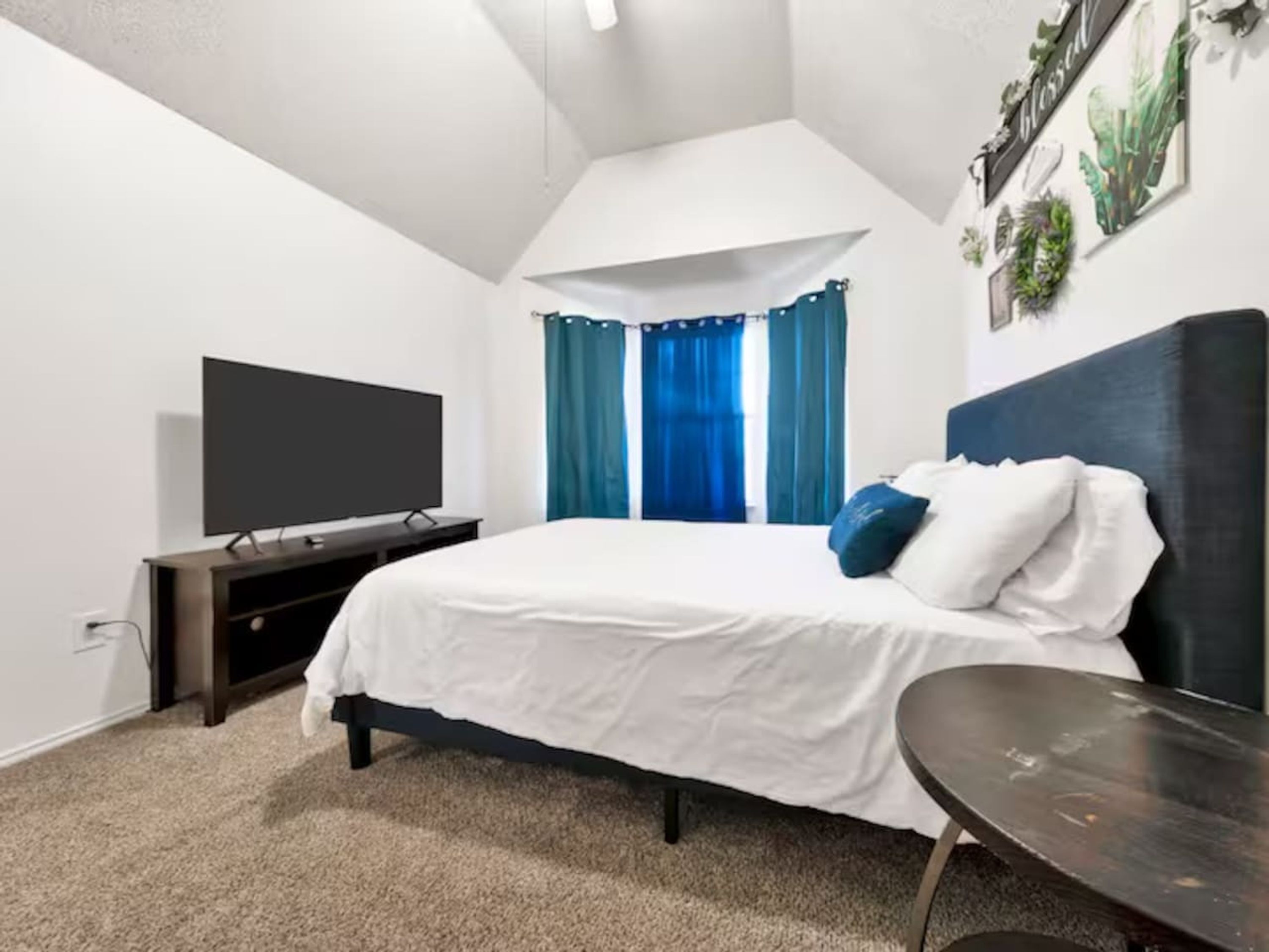 A bedroom with a bed, a TV, a small table, and a window with curtains.