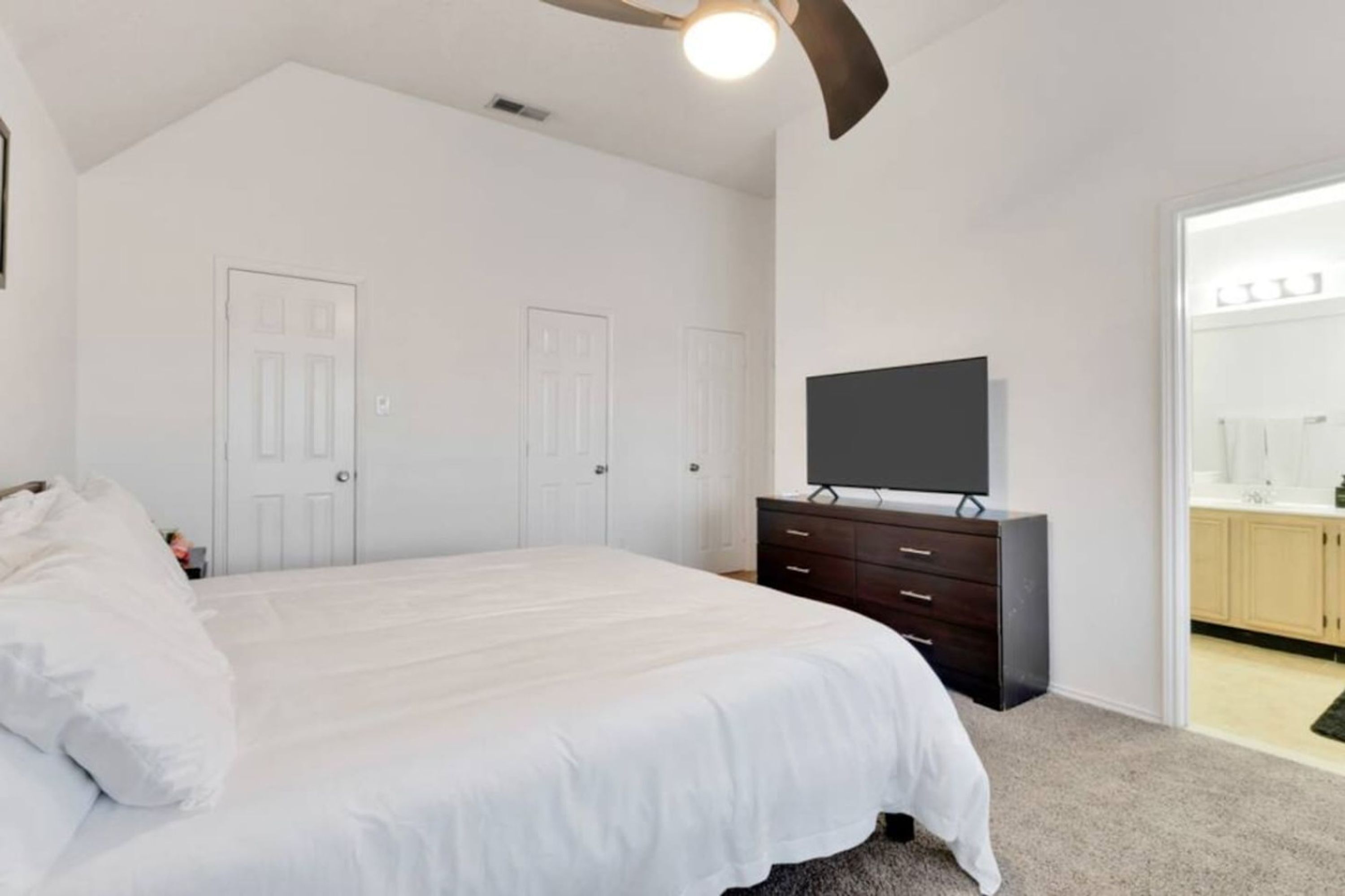 A bedroom with a bed, a dresser, a television, and a door leading to a bathroom.