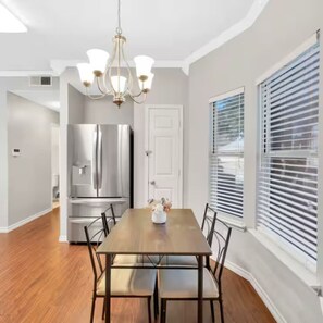 A dining room with a wooden table, chairs, a chandelier, a refrigerator, and a window with blinds. - Frisco Castle 3BR Garage Parking Gated Backyard (Frisco)