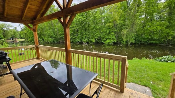 Eine überdachte Terrasse im Freien mit einem Glastisch und Stühlen, mit Blick auf einen Fluss und üppige Vegetation.