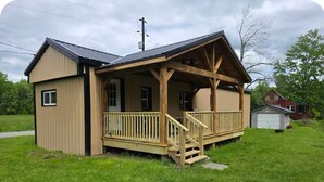 Ein kleines, eingeschossiges Holzhaus mit einer Veranda und einer Treppe, die zu einer Terrasse führt.