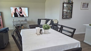 A dining area with a table set for four, a television mounted on the wall, and a cabinet with various items.