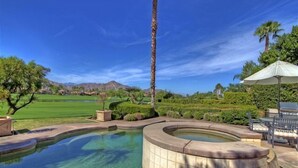 Ein Pool mit geschwungener Form, umgeben von einem angelegten Garten, einer Palme und mit Blick auf einen Golfplatz und Berge im Hintergrund.