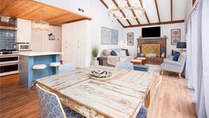 Eine geräumige Küche mit Holzbalkendecke, eine Essecke mit rustikalem Tisch und ein Wohnzimmer mit Kamin.