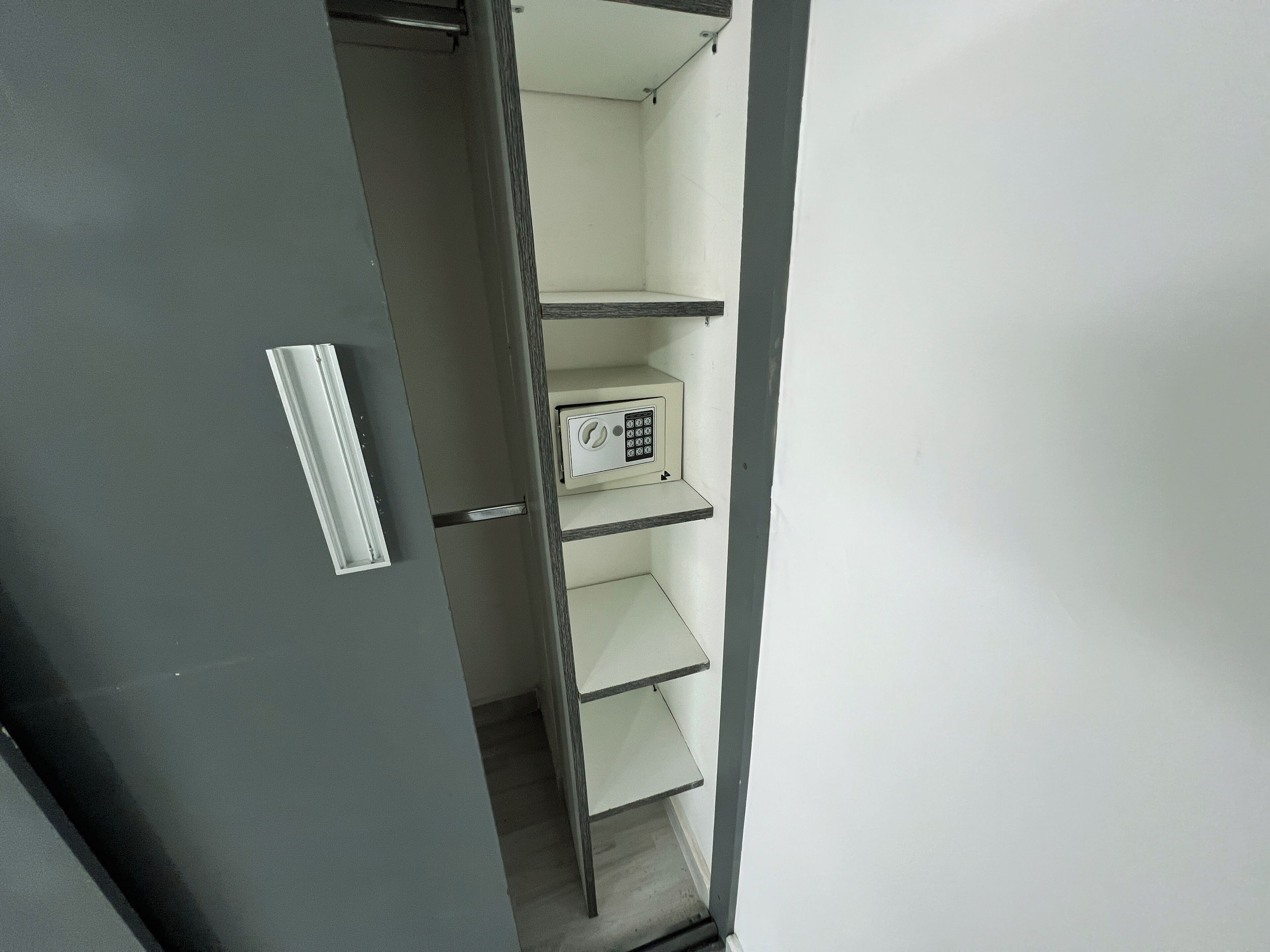 A closed door with a metal handle, a white wall, and a shelf unit with a control panel.