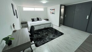 A modern bedroom with a bed, desk, chair, and a small plant.