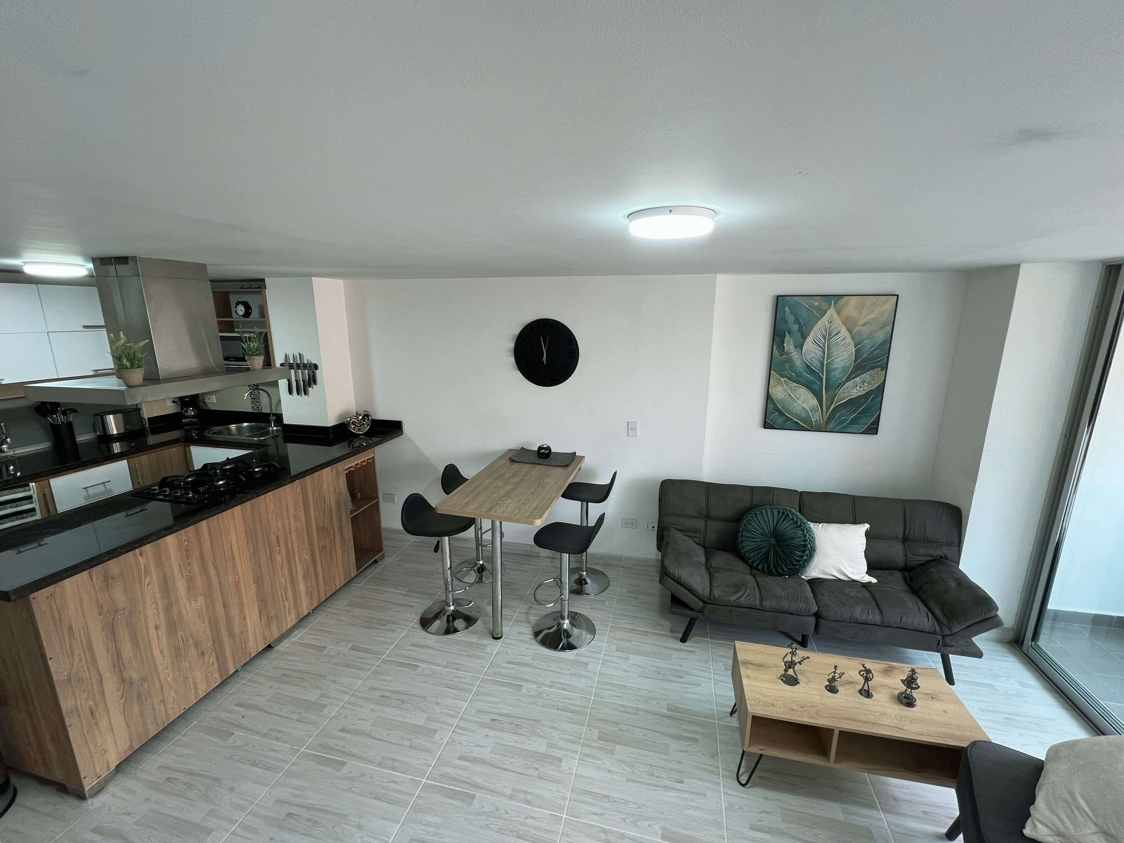 A modern kitchen with a central island, a dining area with chairs, a sofa with a decorative pillow, and a coffee table with figurines.