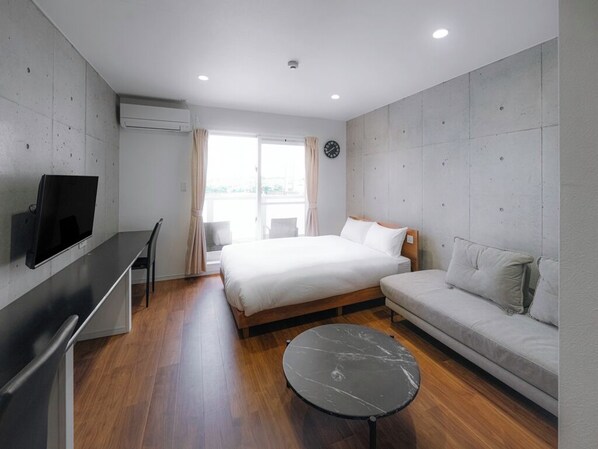 A modern hotel room with a bed, sofa, TV, and a small table. - Meer Residence Hotel Miyako Airport (Miyakojima)