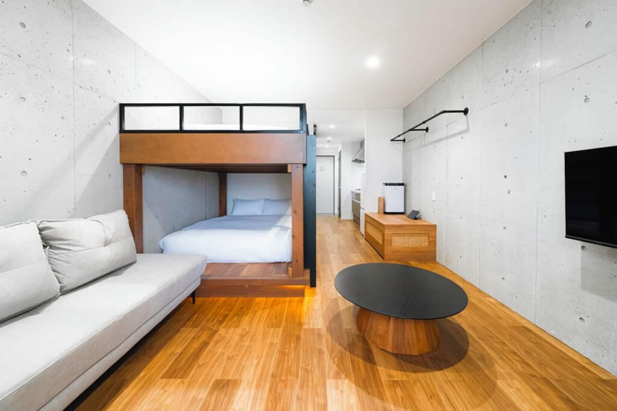 Ein modernes Hotelzimmer mit Etagenbett, einer Schlafcouch, einem runden Couchtisch und einem wandmontierten Flachbildfernseher.