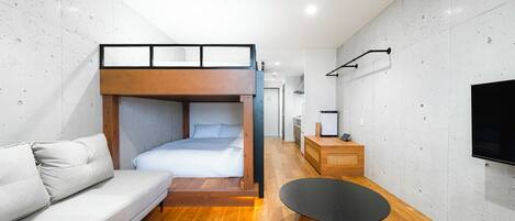 A modern hotel room with a bunk bed, a sofa, a round coffee table, and a flat-screen TV mounted on the wall.