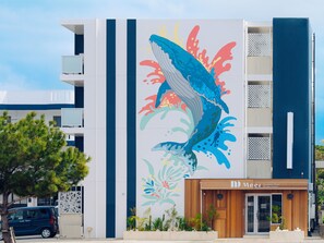 A hotel with a colorful mural of a whale and coral, a wooden facade, and a sign indicating it is the "DD Meer Residence Hotel."