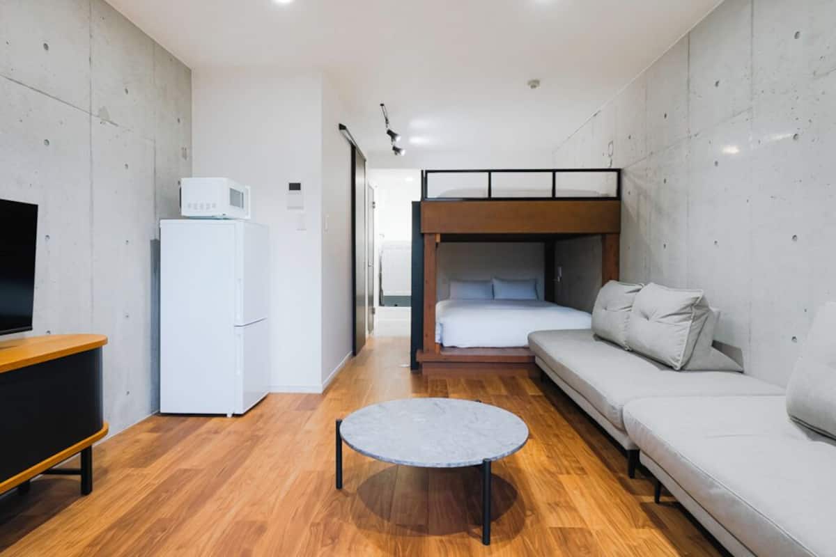 Ein kompaktes Hotelzimmer mit Etagenbett, Schlafsofa, kleinem Tisch, Fernseher und Kühlschrank.