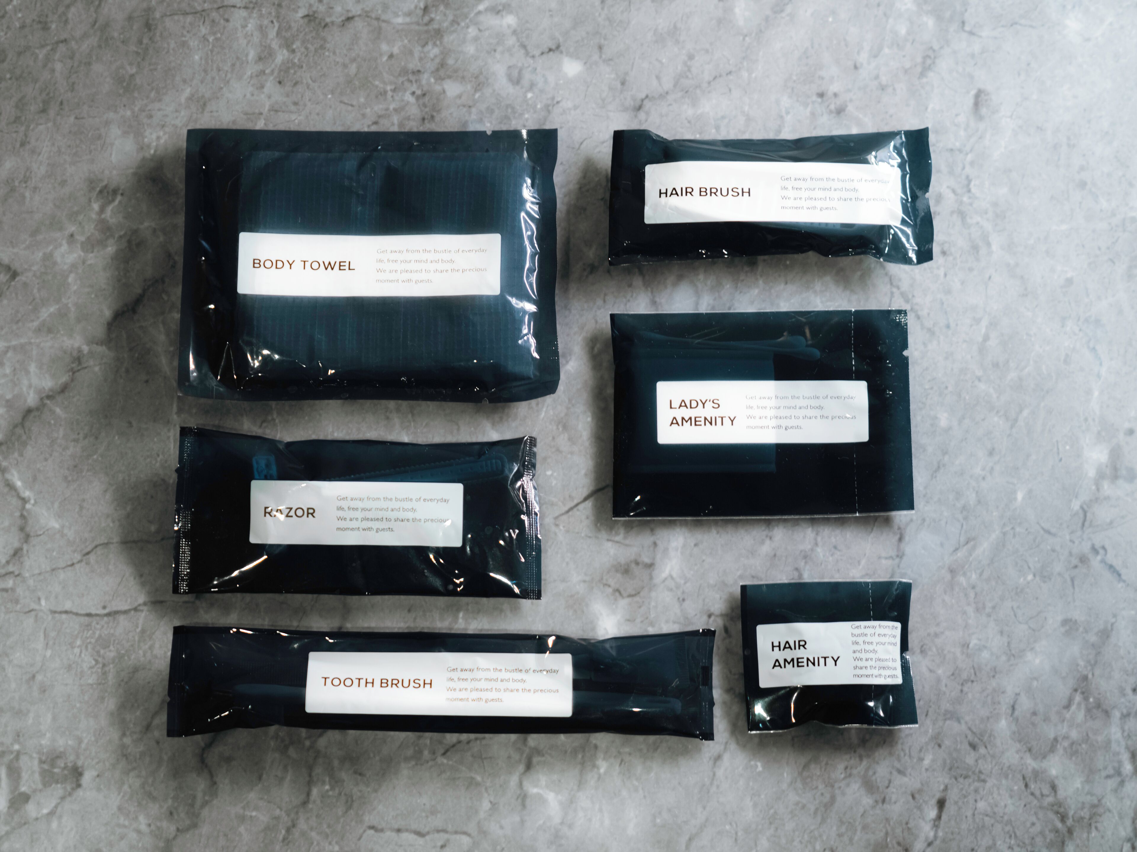 Six black packages labeled with different items: body towel, hair brush, lady's amenity, razor, tooth brush, and hair amenity.