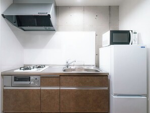 A compact kitchen with a gas stove, oven, microwave, and a sink. - Meer Residence Hotel Miyako Airport (Miyakojima)