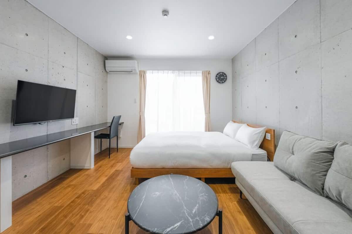 Ein modernes Hotelzimmer mit Bett, Sofa, Fernseher, Schreibtisch und Stuhl.