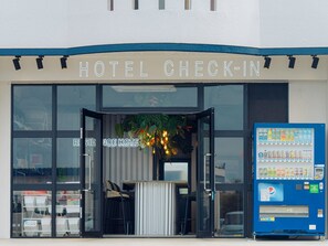 A hotel check-in area with a reception desk, a vending machine, and a large window. - Meer ResidenceHotel MiyakoAirport (Miyakojima)