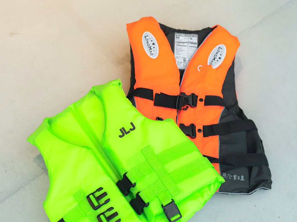 Two life vests, one bright green and one orange, with reflective strips and safety labels.