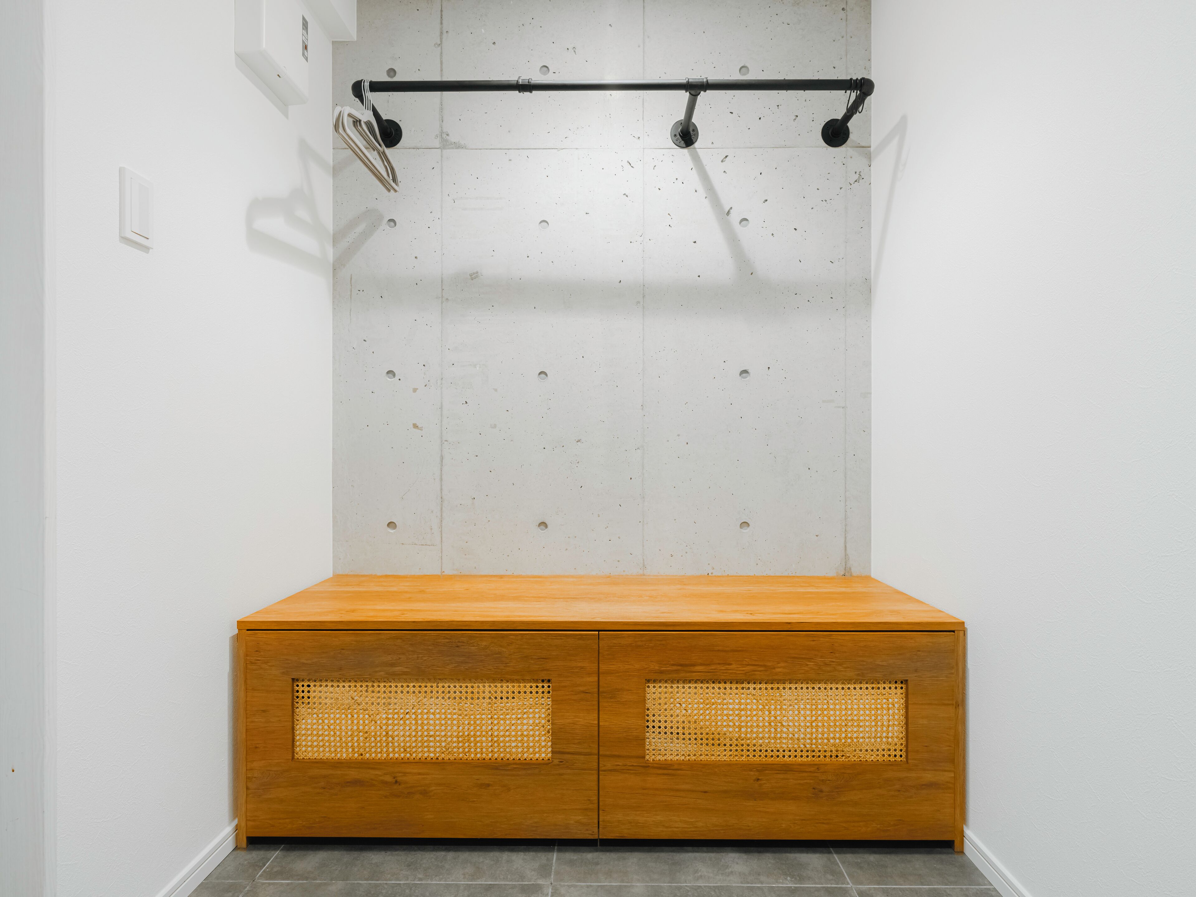Ein Zimmer mit einem Holzschrank mit Geflechtüren, einer weißen Wand mit einer Lochplatte und einer Deckenstange.