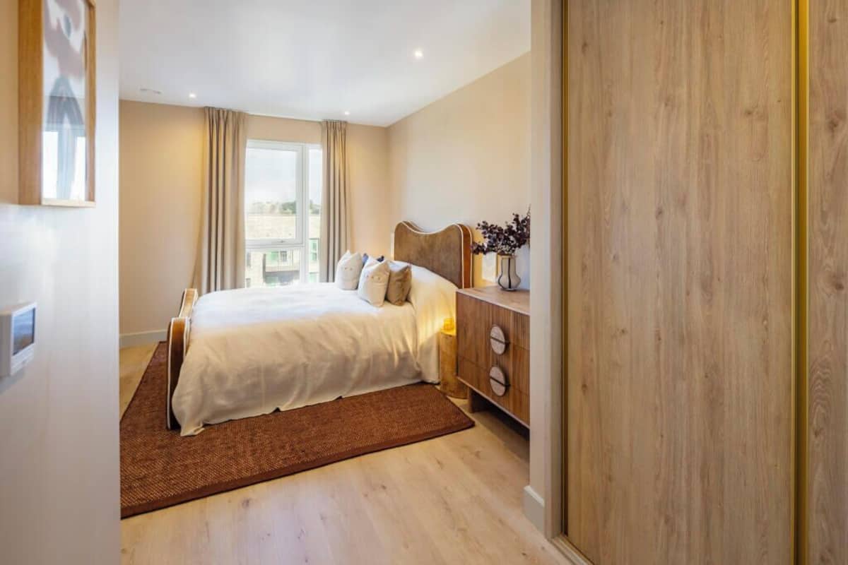 A bedroom with a bed, wooden dresser, and a view of the city.