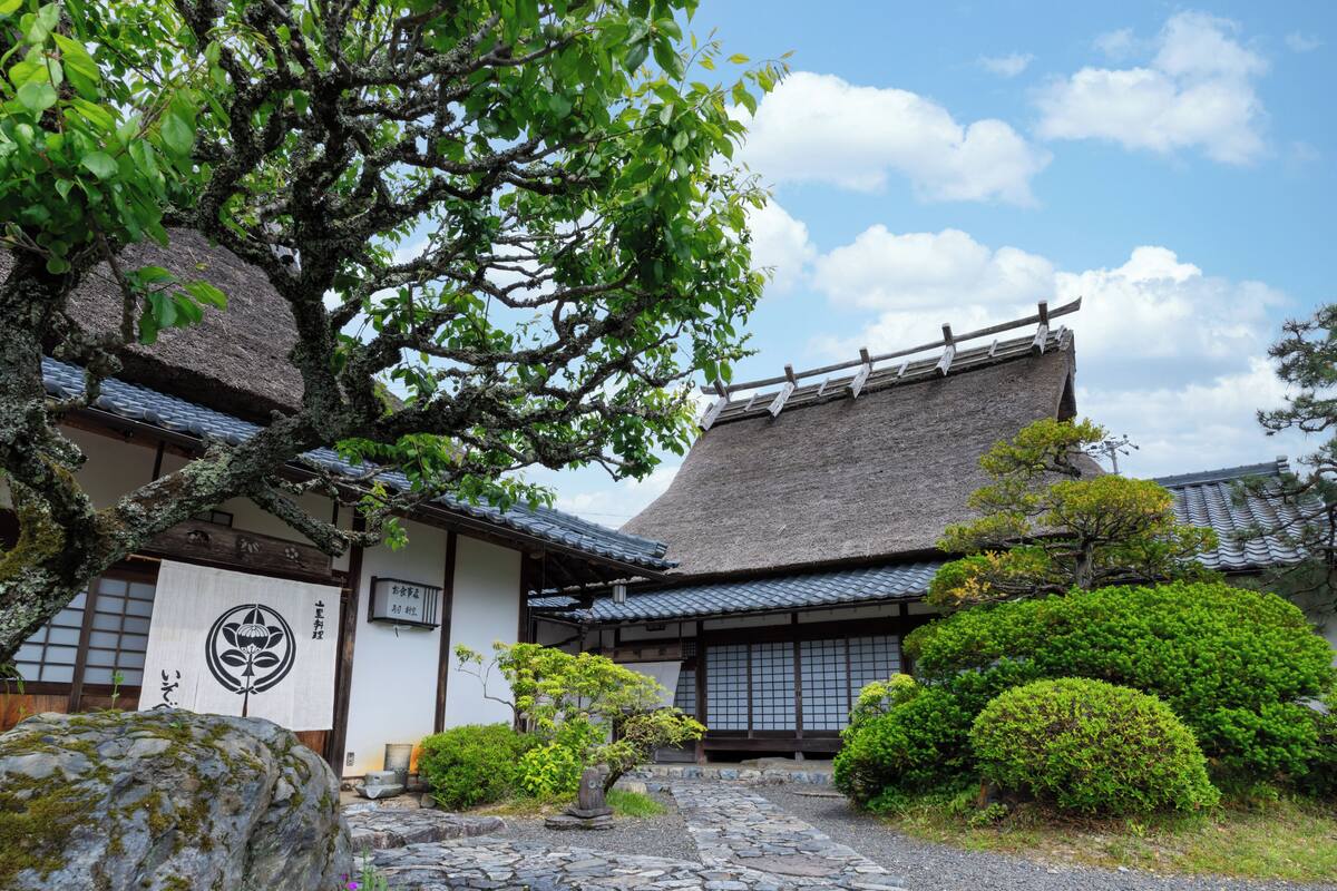 A traditional Japanese building with a thatched roof, surrounded by well-maintained greenery and stone pathways.