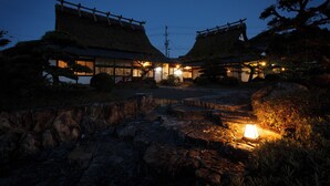 A traditional Japanese building with a thatched roof, stone pathway, and a small illuminated lantern. - Ryori Ryokan Yamazato Ryori Isobe (Nantan)