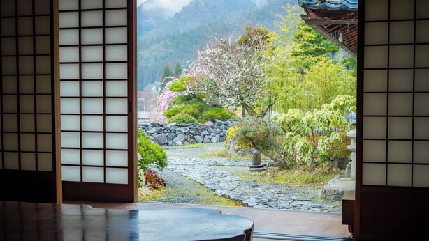 A traditional Japanese room with tatami flooring, a low table, and a view of a garden with a stone path, trees, and a mountain backdrop. - Ryori Ryokan Yamazato Ryori Isobe (Nantan)