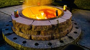 A circular stone fire pit with a metal rim, surrounded by a concrete base with holes. - The Horse Inn Around @ Spring Brook Resort (Wisconsin Dells)