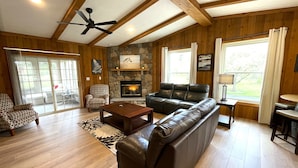 A living room with a fireplace, leather sofa, patterned armchair, and wooden floors. - The Horse Inn Around @ Spring Brook Resort (Wisconsin Dells)