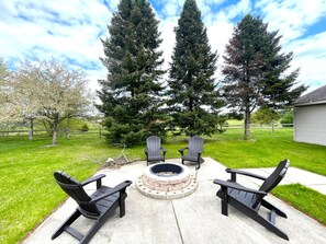 An outdoor seating area with Adirondack chairs, a fire pit, and tall evergreen trees. - The Horse Inn Around @ Spring Brook Resort (Wisconsin Dells)