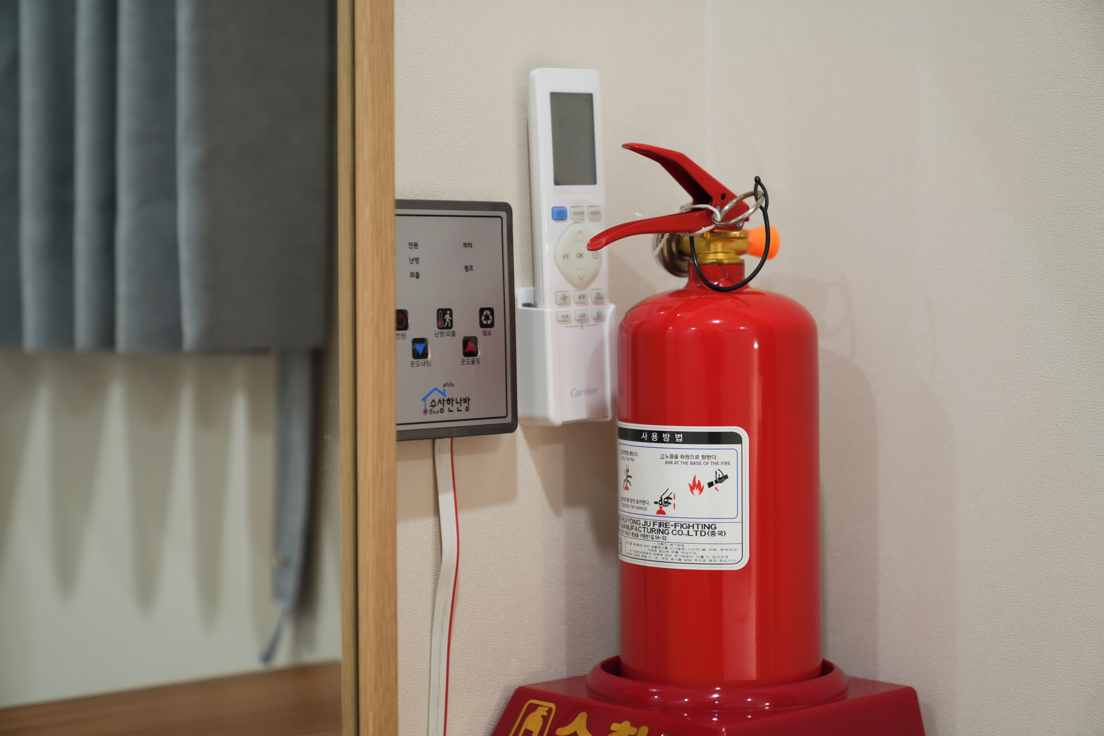 Een rode brandblusser bevestigd aan een muur, naast een bedieningspaneel met een digitaal scherm.