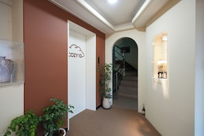 Un pasillo con una puerta identificada como 'COZY10', una escalera y plantas en macetas.