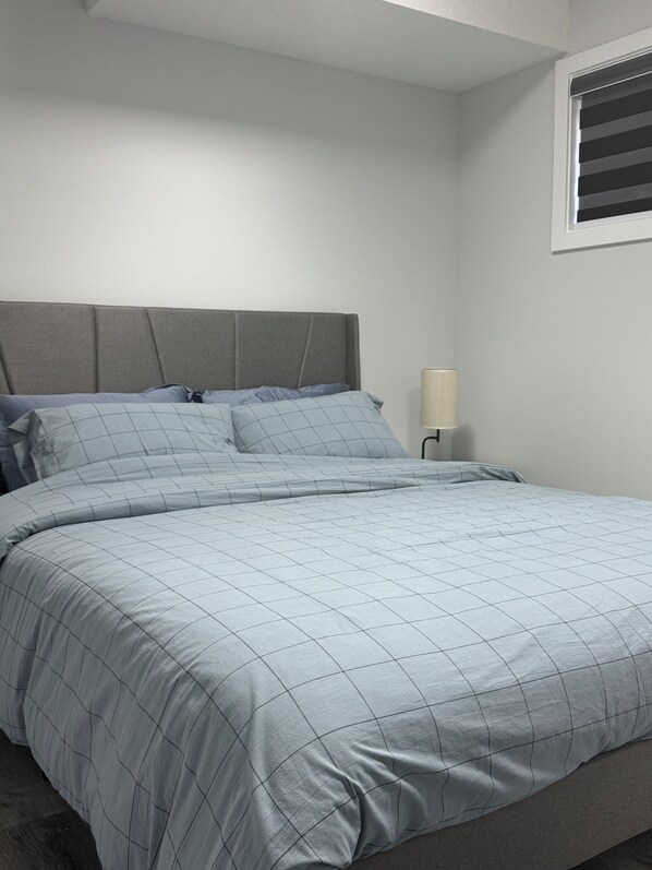 Ein ordentlich bezogenes Bett mit grauem Kopfteil und einer hellblauen, gesteppten Bettdecke.