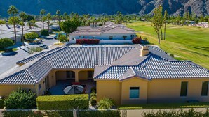 A residential area with a house featuring a tiled roof, a patio with outdoor furniture, and a view of a golf course and mountains in the background.