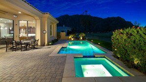 A pool area with a view of mountains, a dining area with outdoor furniture, and a building with a tiled roof.