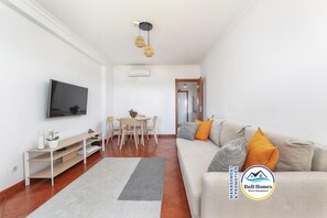 Un salon moderne comprenant un canapé, un téléviseur et un coin repas avec une table et des chaises.