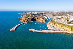 An aerial view of a coastal town with a marina, rocky cliffs, and a mix of residential and commercial buildings.