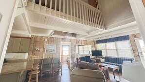 Een ruime woonkamer met een hoge plafond, een balkon en een eethoek met barstoelen.