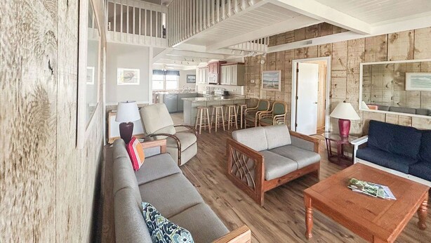 Een ruime woonkamer met een hoge nok, houten vloeren en een keuken op de achtergrond.