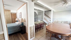 Een slaapkamer met een bed, nachtkastje en lamp. Er is een eethoek met een tafel en stoelen.