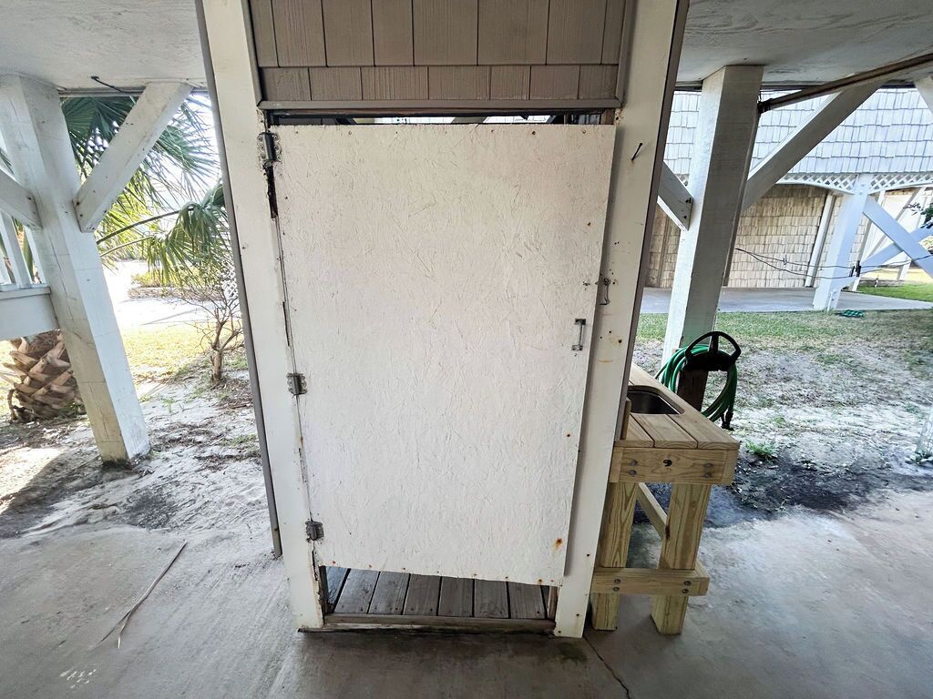 A covered outdoor area with a white door, wooden steps, and a concrete floor.