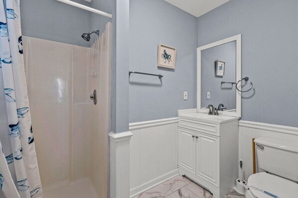 A bathroom with a shower, toilet, sink, and a mirror.