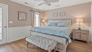 A bedroom with a large bed, a bench, a nightstand, a ceiling fan, and a window with curtains. - Endless Summer-Spacious 5BR Retreat Steps from Cherry Grove Beach! (North Myrtle Beach)