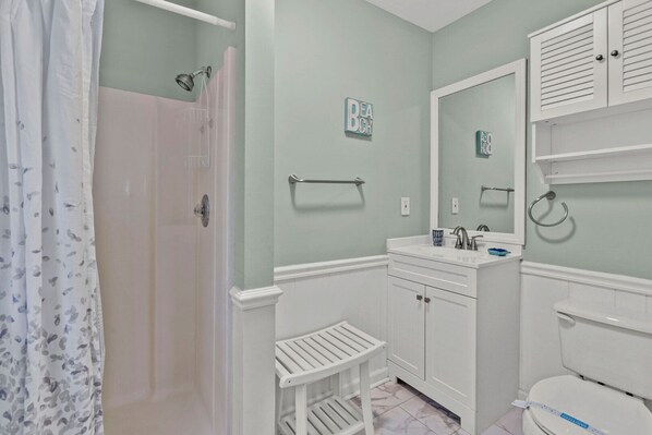 A bathroom with a shower, toilet, and sink. There is a towel rack, a small stool, and a mirror above the sink. - Endless Summer-Spacious 5BR Retreat Steps from Cherry Grove Beach! (North Myrtle Beach)