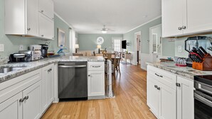A modern kitchen with white cabinets, a dishwasher, a stove, and a coffee maker. - Endless Summer-Spacious 5BR Retreat Steps from Cherry Grove Beach! (North Myrtle Beach)