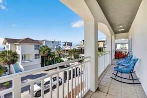 A balcony with a view of neighboring houses, a white fence, and blue rocking chairs.