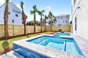 A swimming pool with a wooden fence, palm trees, and a white building in the background.