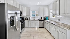 A modern kitchen with white cabinetry, stainless steel appliances, and a marble countertop.