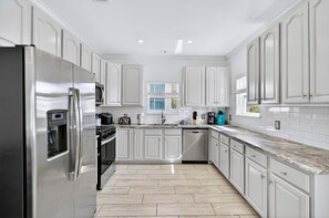 A modern kitchen with white cabinetry, stainless steel appliances, and a marble countertop.